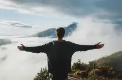 A person with open arms above a sea of clouds