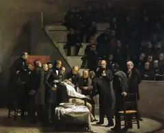 Oil painting: doctors in dark frock coats surround an anaesthetised patient in a surgical chair, before a crowded tiered theatre.